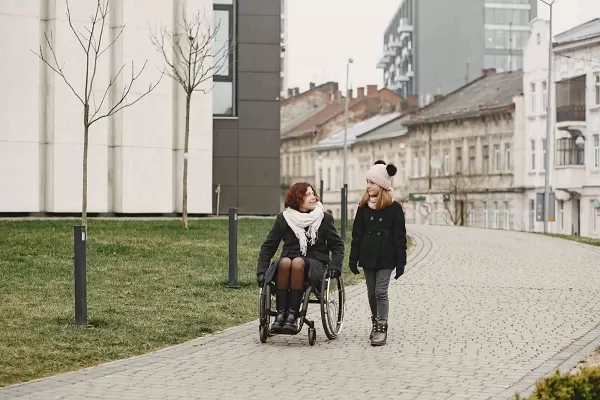 Vrouw met een handicap in een rolstoel met haar dochter die buiten in een park loopt.