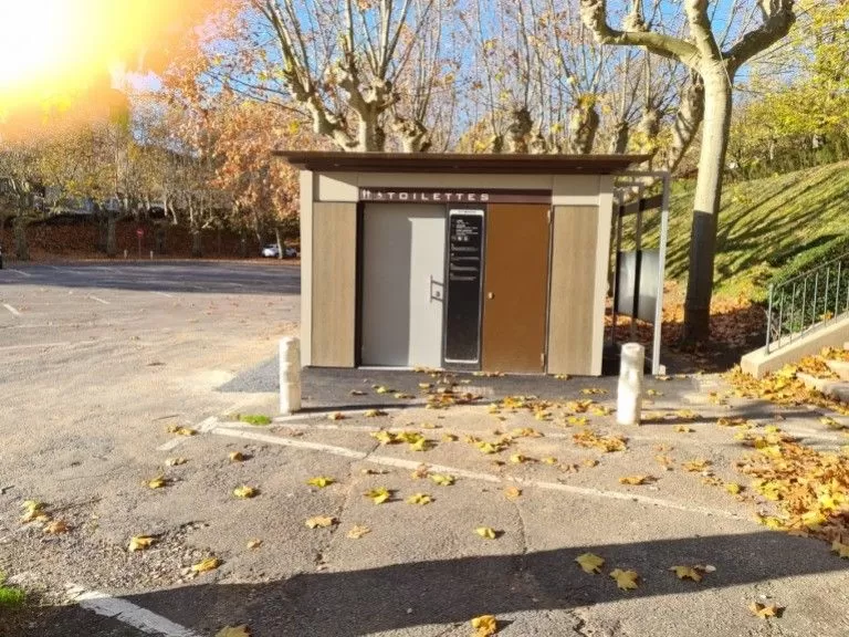 Beige en houten openbare toiletten op een parkeerterrein in Bourg-en-Bresse